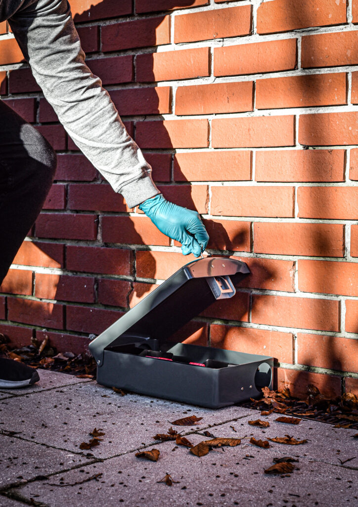 pest controller opening a humane metal rat box to service it, outside an athens ga commercial building