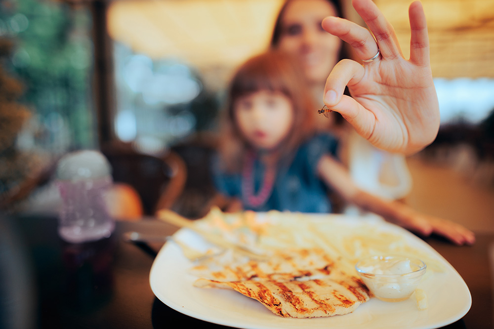 Woman holding insect over child’s plate of food
